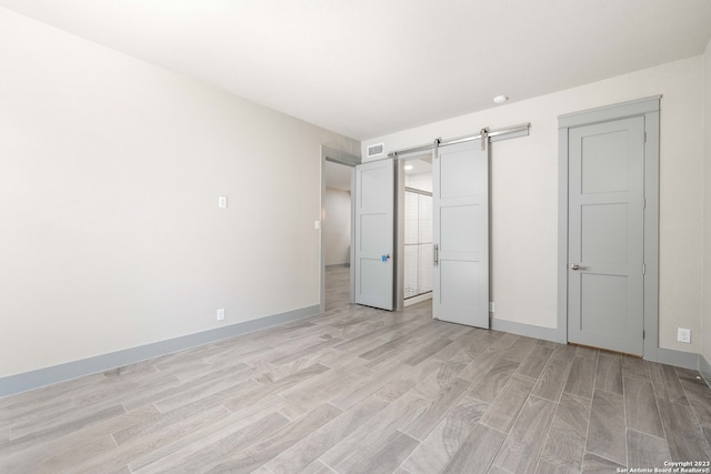 unfurnished bedroom featuring a barn door and light hardwood / wood-style flooring