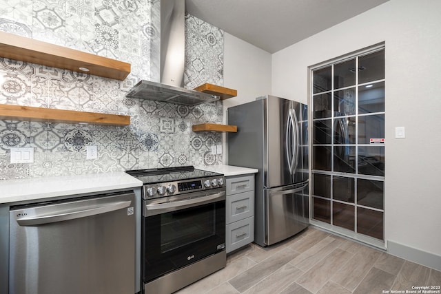 kitchen with gray cabinets, tasteful backsplash, stainless steel appliances, and wall chimney exhaust hood