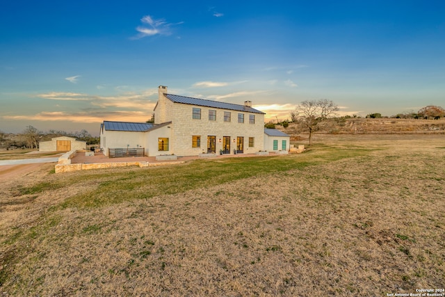 back house at dusk with a yard, an outdoor structure, and a patio