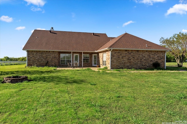 back of house with an outdoor fire pit and a yard