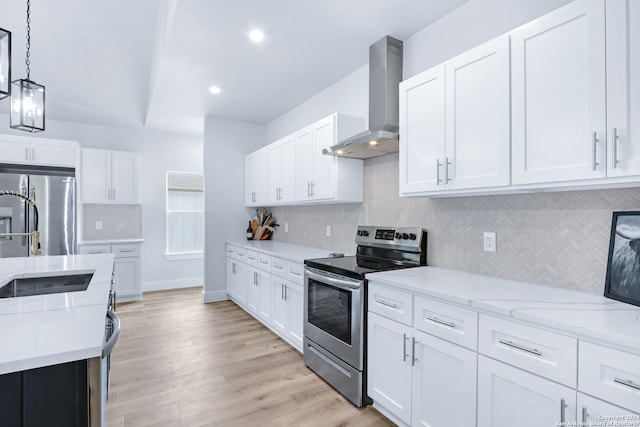 kitchen featuring pendant lighting, light hardwood / wood-style floors, stainless steel appliances, wall chimney exhaust hood, and white cabinets