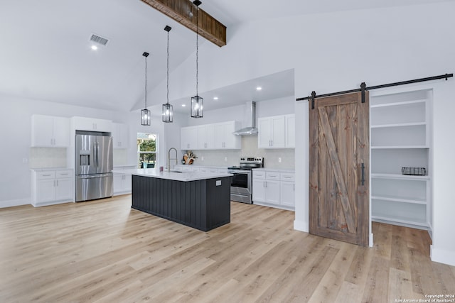 kitchen with wall chimney range hood, a barn door, light hardwood / wood-style floors, and appliances with stainless steel finishes