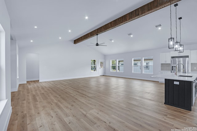 unfurnished living room with beam ceiling, ceiling fan, sink, and light wood-type flooring