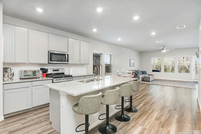 kitchen with a kitchen island with sink, ceiling fan, sink, stainless steel appliances, and light wood-type flooring