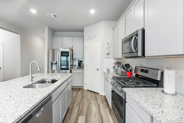 kitchen with light stone countertops, appliances with stainless steel finishes, sink, light wood-type flooring, and tasteful backsplash