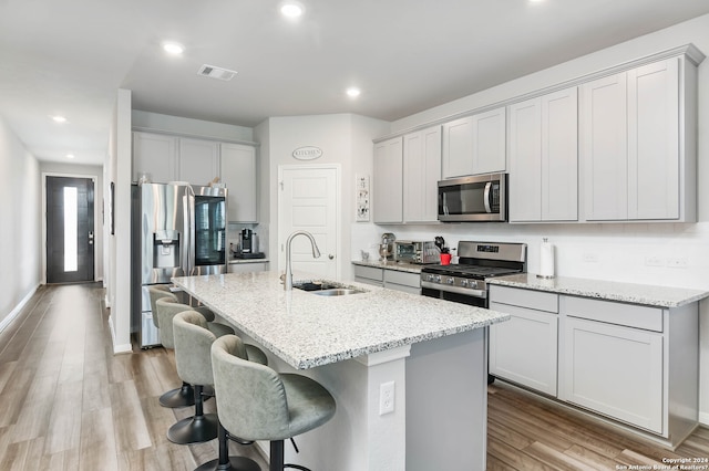 kitchen featuring an island with sink, stainless steel appliances, light hardwood / wood-style floors, light stone countertops, and sink