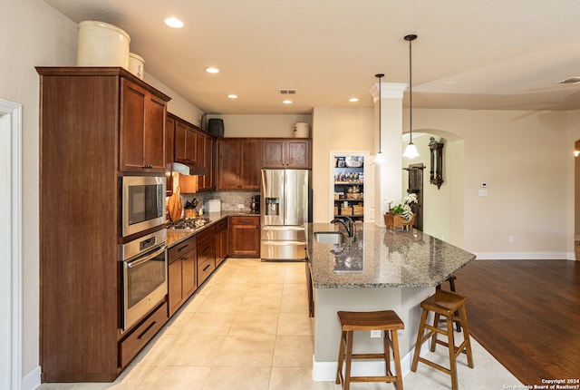 kitchen with dark stone countertops, stainless steel appliances, decorative light fixtures, custom exhaust hood, and a kitchen bar