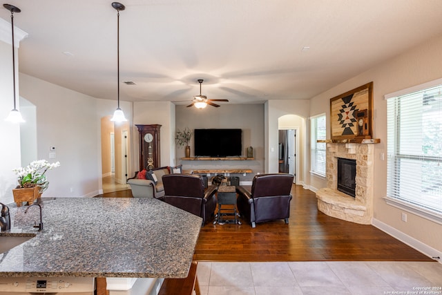 living room featuring ceiling fan, wood-type flooring, and a stone fireplace