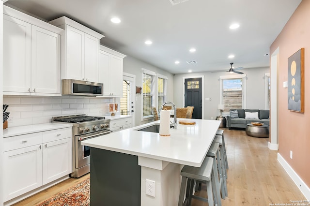 kitchen with appliances with stainless steel finishes, tasteful backsplash, light hardwood / wood-style floors, a kitchen bar, and ceiling fan