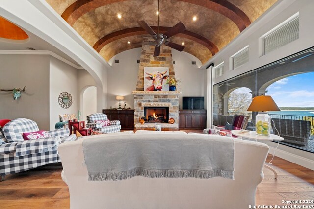 living room with high vaulted ceiling, ceiling fan, a stone fireplace, and light hardwood / wood-style flooring