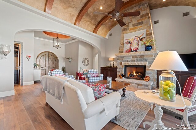 living room with beamed ceiling, a fireplace, high vaulted ceiling, ceiling fan with notable chandelier, and hardwood / wood-style flooring