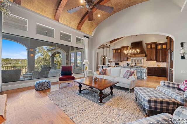 living room with high vaulted ceiling, ceiling fan with notable chandelier, and light hardwood / wood-style flooring