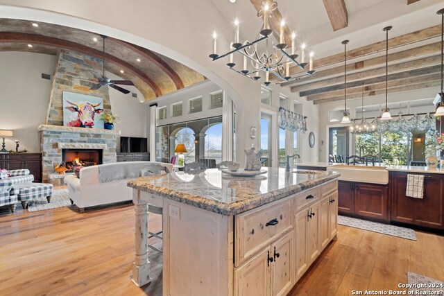 kitchen with a kitchen island with sink, a breakfast bar, light hardwood / wood-style floors, ceiling fan with notable chandelier, and a stone fireplace