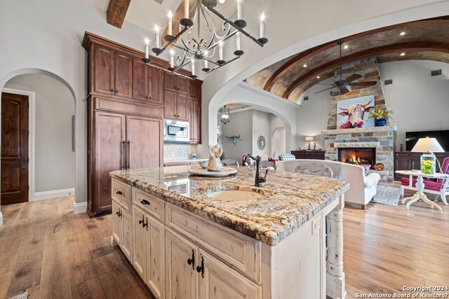 kitchen with a kitchen island with sink, a fireplace, light stone countertops, and light wood-type flooring