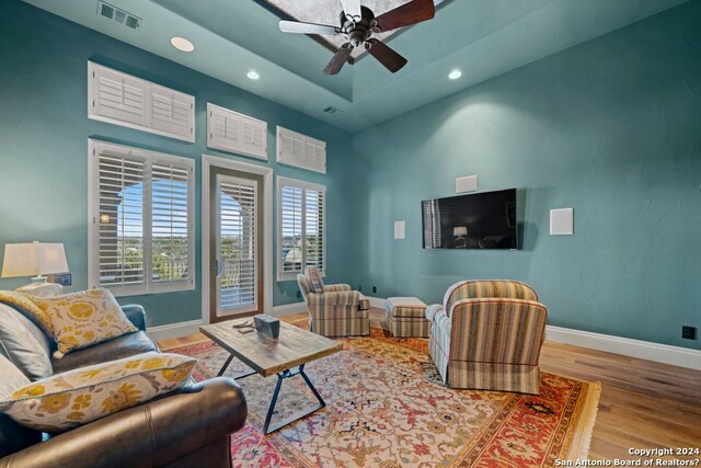 living room with light hardwood / wood-style flooring, a tray ceiling, and ceiling fan