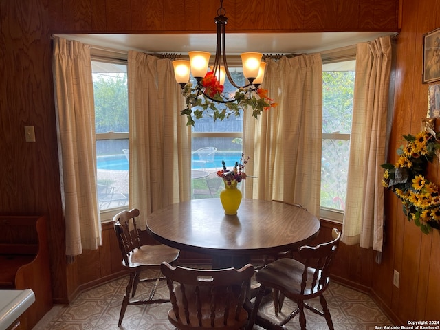 dining space featuring an inviting chandelier, wooden walls, and a healthy amount of sunlight