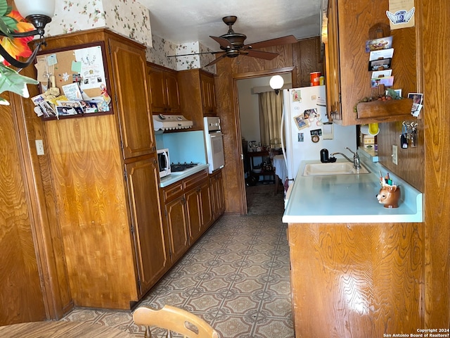 kitchen with white appliances, wooden walls, ceiling fan, light tile floors, and sink