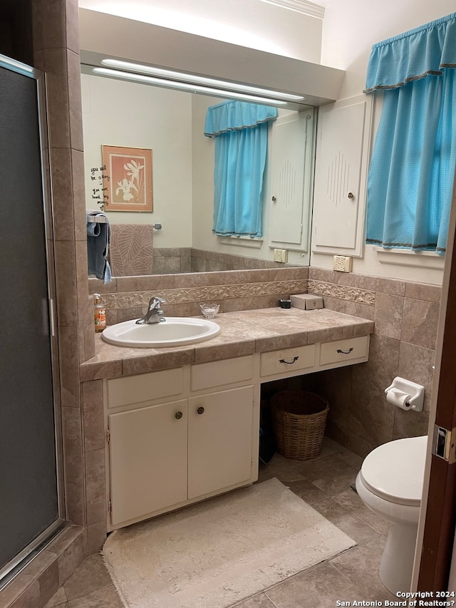 bathroom with tile walls, toilet, a shower with shower door, tile floors, and vanity