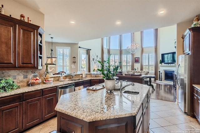 kitchen with a notable chandelier, light stone countertops, tasteful backsplash, a center island with sink, and light wood-type flooring