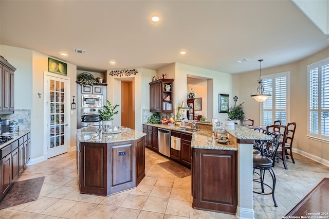 kitchen featuring hanging light fixtures, backsplash, stainless steel appliances, a center island, and light stone counters