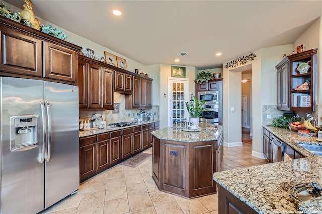 kitchen with a kitchen island, tasteful backsplash, appliances with stainless steel finishes, and light stone countertops