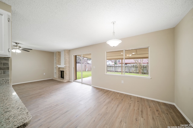 unfurnished living room with ceiling fan, a brick fireplace, light hardwood / wood-style floors, and a textured ceiling