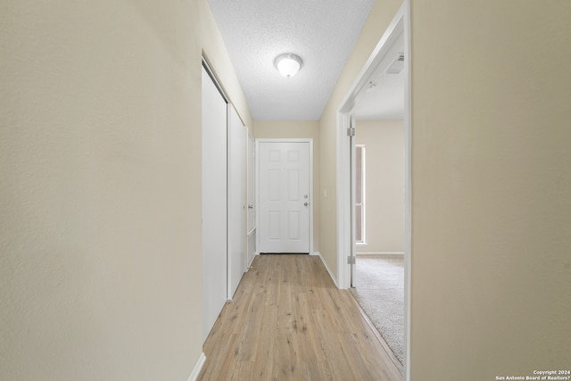 hallway with light hardwood / wood-style flooring and a textured ceiling