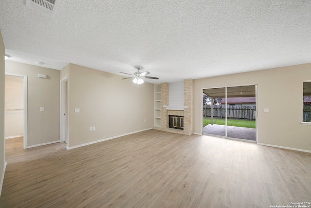 unfurnished living room featuring light hardwood / wood-style floors, a textured ceiling, ceiling fan, and a brick fireplace