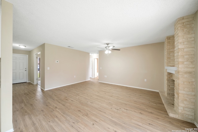 unfurnished living room featuring brick wall, a brick fireplace, ceiling fan, light hardwood / wood-style floors, and a textured ceiling