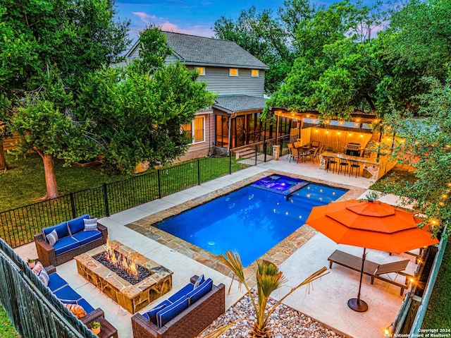 pool at dusk featuring an outdoor living space with a fire pit, an outdoor bar, an in ground hot tub, a lawn, and a patio area