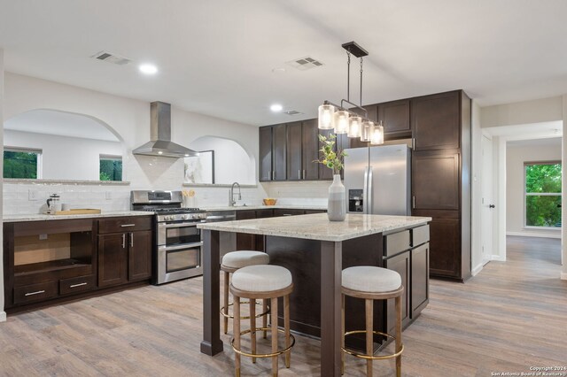 kitchen with light wood-type flooring, a kitchen island, decorative light fixtures, stainless steel fridge, and a breakfast bar area