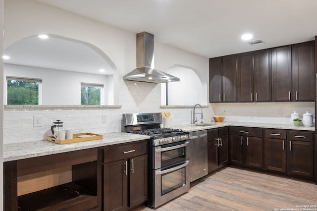 kitchen featuring decorative backsplash, light hardwood / wood-style floors, appliances with stainless steel finishes, and wall chimney exhaust hood