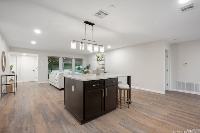 kitchen featuring dark brown cabinets, pendant lighting, light hardwood / wood-style flooring, and light stone counters