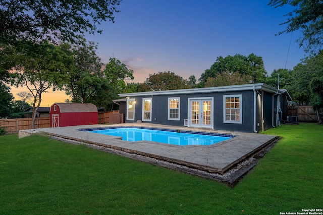 pool at dusk with a storage shed, central air condition unit, french doors, and a lawn