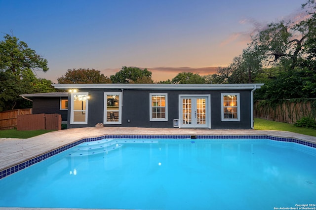 pool at dusk featuring french doors and a patio area