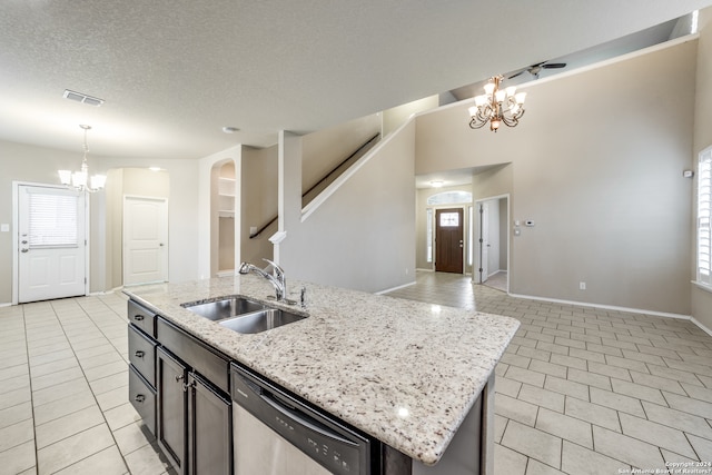 kitchen with sink, light tile floors, a center island with sink, stainless steel dishwasher, and pendant lighting