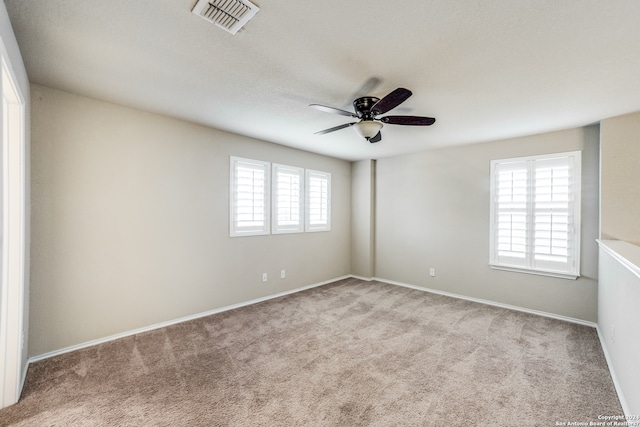 empty room featuring ceiling fan, a wealth of natural light, and light carpet