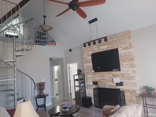 living room featuring ceiling fan, a fireplace, a towering ceiling, and light hardwood / wood-style floors