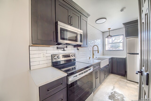 kitchen with sink, stainless steel appliances, light stone countertops, tasteful backsplash, and decorative light fixtures