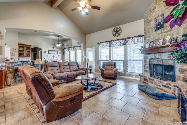 living room featuring ceiling fan, beam ceiling, a stone fireplace, and high vaulted ceiling