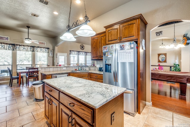 kitchen with ceiling fan with notable chandelier, a center island, stainless steel appliances, and pendant lighting