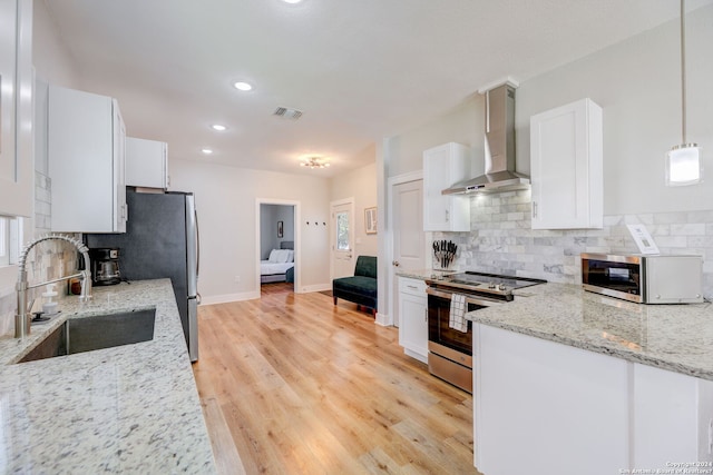 kitchen featuring appliances with stainless steel finishes, backsplash, wall chimney exhaust hood, and light hardwood / wood-style flooring