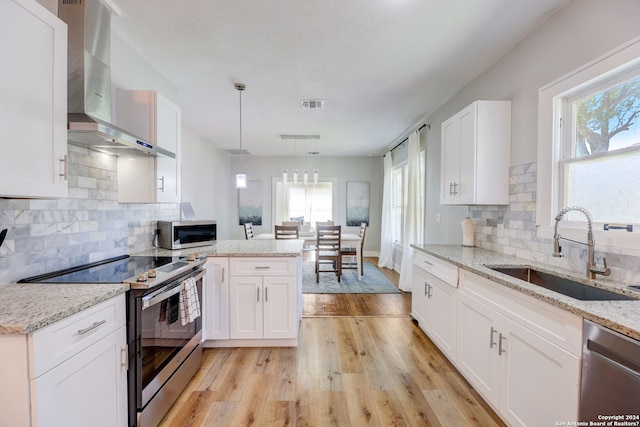 kitchen with white cabinetry, sink, light hardwood / wood-style flooring, stainless steel appliances, and wall chimney range hood