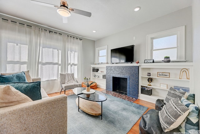 living room with light hardwood / wood-style floors, a tiled fireplace, ceiling fan, and built in shelves