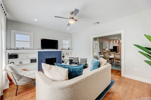 living room featuring a healthy amount of sunlight, a tile fireplace, ceiling fan, and light hardwood / wood-style flooring