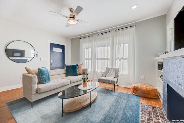 living room with ceiling fan, hardwood / wood-style flooring, and a tiled fireplace