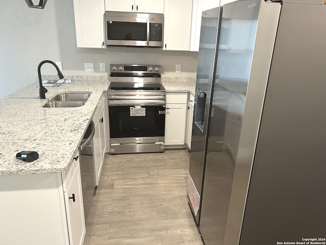 kitchen with light stone countertops, sink, light hardwood / wood-style floors, white cabinets, and appliances with stainless steel finishes