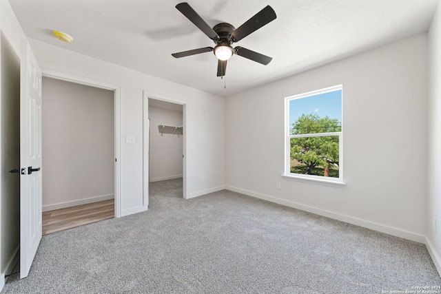 unfurnished bedroom featuring carpet, a walk in closet, a closet, and ceiling fan