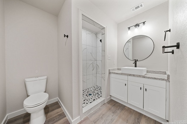 bathroom with tiled shower, hardwood / wood-style floors, vanity, and toilet