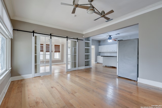 unfurnished room with light hardwood / wood-style flooring, a wealth of natural light, ceiling fan, and a barn door